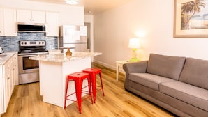 A compact kitchen with a central island, red bar stools, a grey sofa, and a framed picture on the wall. - Beach Condo & Pool Relaxing Getaway! Short Stride to Sandy Beach's. Unit 8 (Panama City Beach)