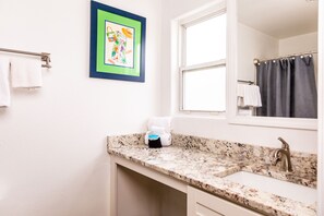 A bathroom with a granite countertop, a sink, a mirror, a window, and a towel rack.