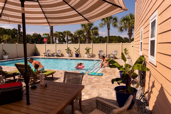 A backyard with a swimming pool, lounge chairs, and potted plants.