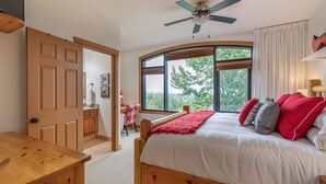 Een slaapkamer met een houten bed, een bureau en een stoel. Er is een raam met uitzicht op bomen en bergen.