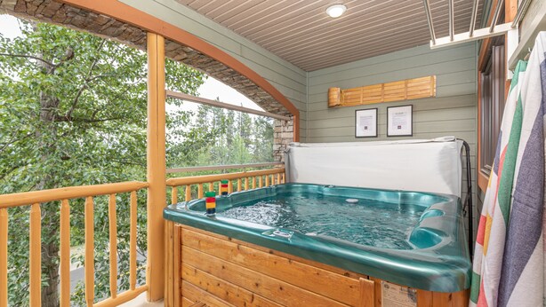 Een houten jacuzzi op een balkon met uitzicht op bomen, een houten leuning en een plafond met een lamp.