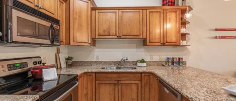 A kitchen with wooden cabinets, a stainless steel microwave, a stove, and granite countertops.