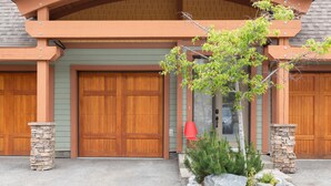 Een huis met twee verdiepingen, een stenen zuil, een houten garagepoort en een kleine boom in de voortuin.