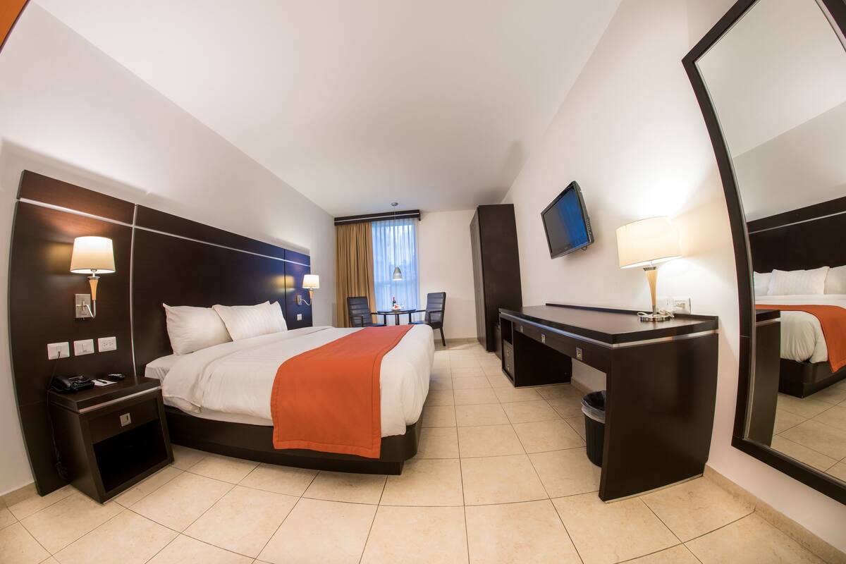 A hotel room with a bed, desk, and a TV.