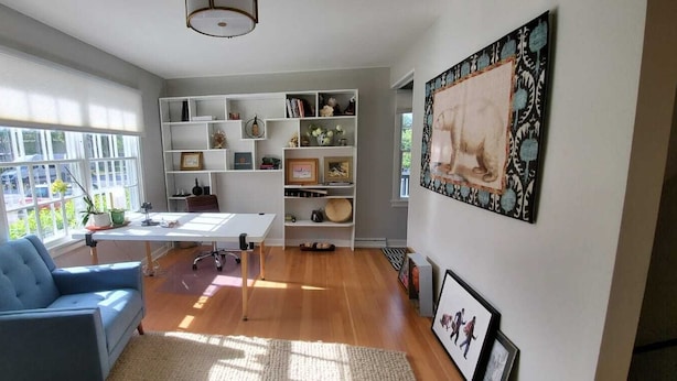 Una habitación con escritorio, sofá azul, estantería y un cuadro grande en la pared.