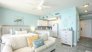 Ein Schlafzimmer mit einem Bett, einem weißen Sofa, einem Deckenventilator und einer Küchenzeile im Hintergrund.