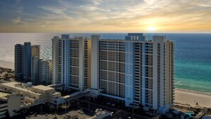 Ein Hochhaus-Hotel mit mehreren Etagen, Blick auf den Strand und einem Sonnenuntergang im Hintergrund.
