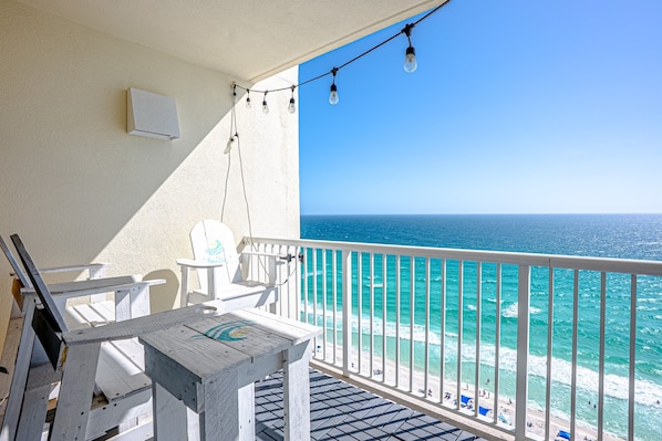 A balcony with a view of the ocean, a table, chairs, and string lights.