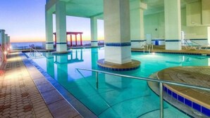 Ein Poolbereich mit klarem, blauem Wasser, einer gefliesten Liegefläche und Blick auf den Ozean im Abendrot.