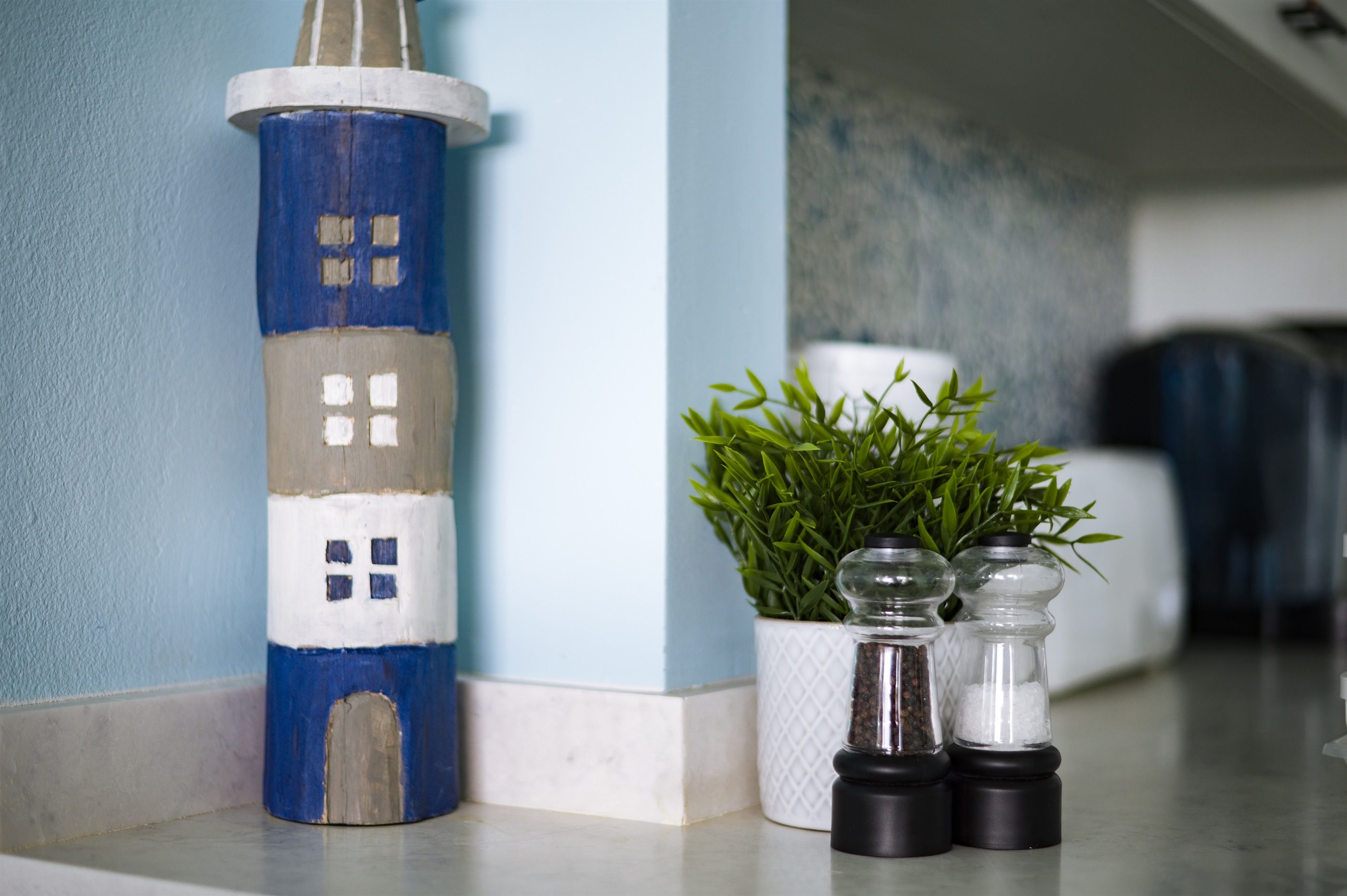 A small, painted lighthouse model next to a potted plant and two salt shakers on a kitchen counter.