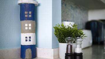 A small, painted lighthouse model next to a potted plant and two salt shakers on a kitchen counter.