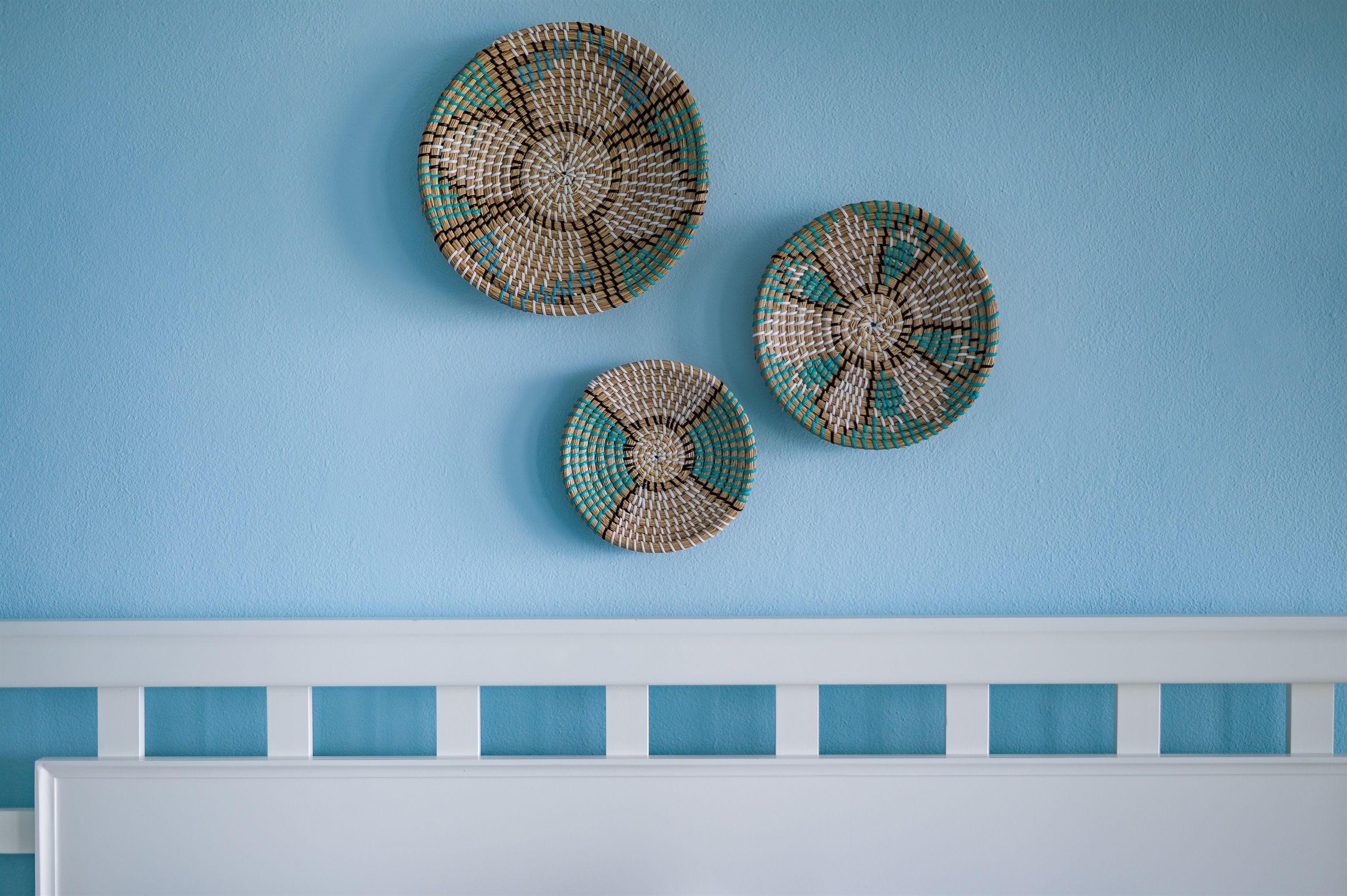 Three woven wall hangings on a blue wall.