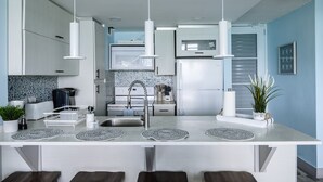 A modern kitchen with white cabinetry, a central island with a sink, and pendant lighting. - Oceanfront Condo • Pool • Near Seven Seas Beach (Fajardo)
