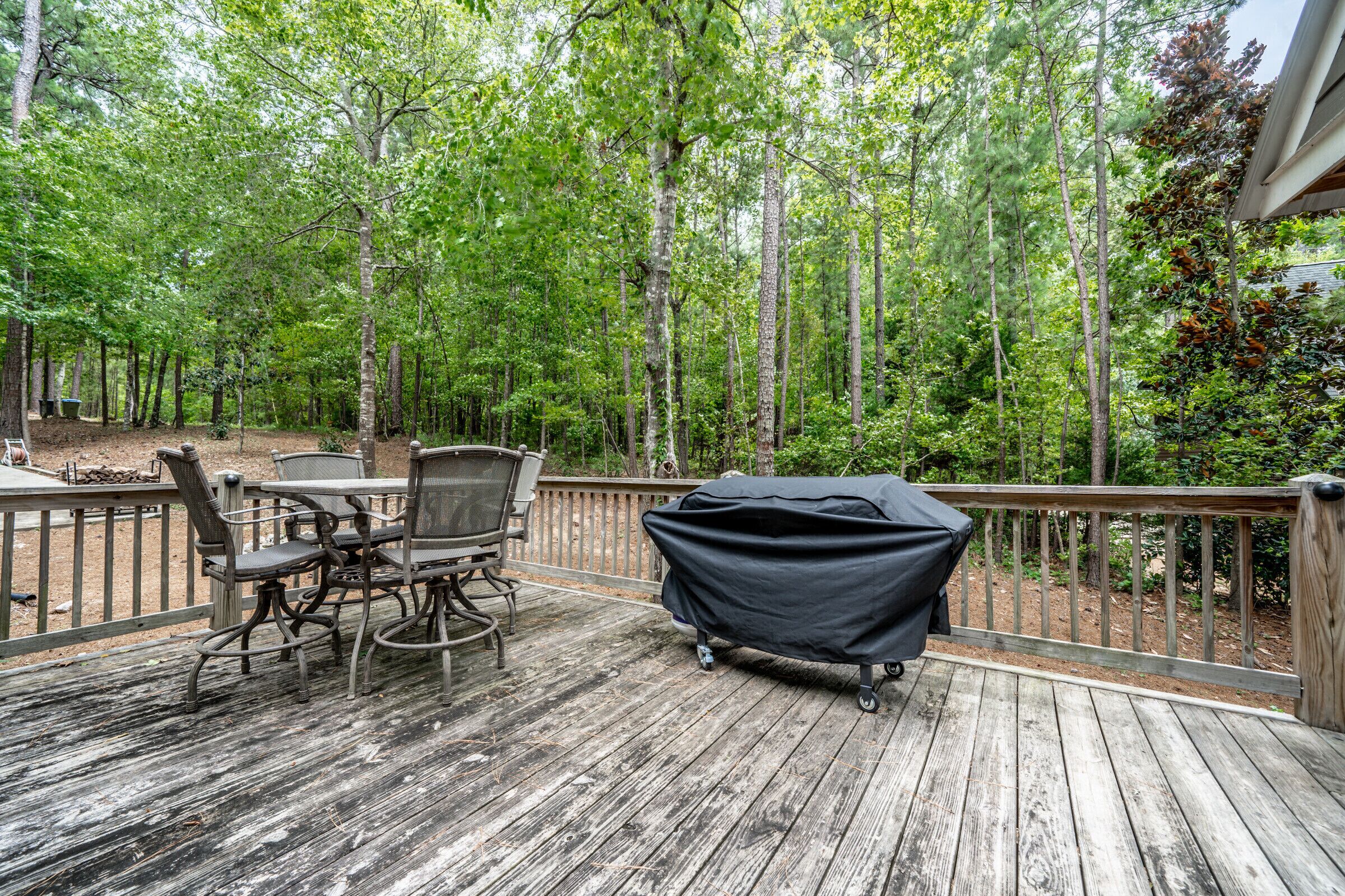 Une terrasse en bois avec une table et des chaises, entourée d’une forêt.