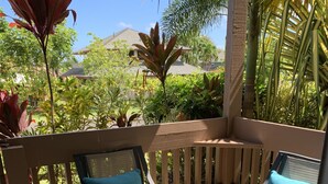 Une table ronde en verre, entourée de quatre chaises, chacune dotée d’un coussin de couleur turquoise, sur une terrasse en bois avec une rambarde.