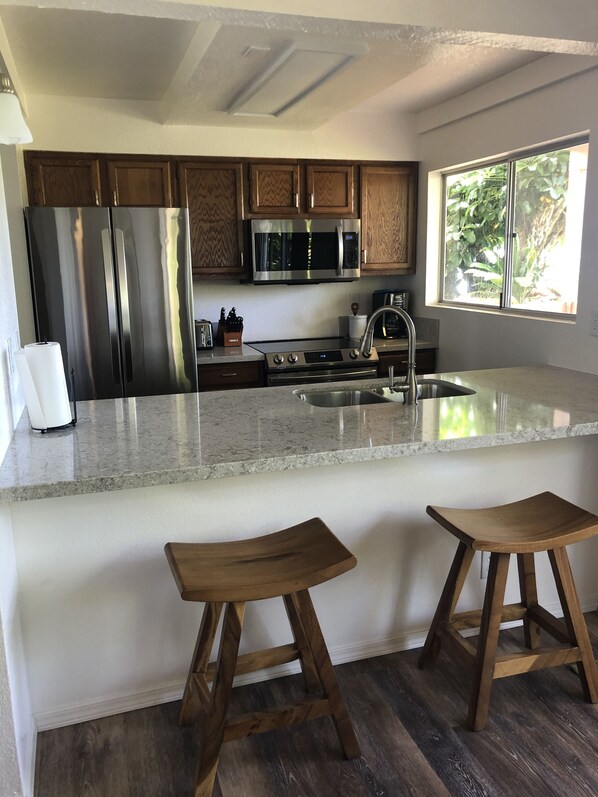 A modern kitchen with stainless steel appliances, wooden cabinets, and a large window.
