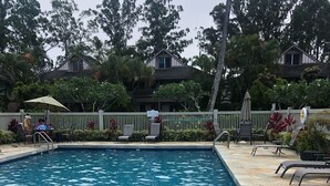 Une piscine rectangulaire avec une terrasse carrelée, entourée d’une clôture blanche et d’une végétation luxuriante.