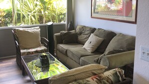 Un salon comprenant un canapé, deux fauteuils, une table basse et une grande fenêtre donnant sur un paysage verdoyant.