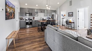 A modern kitchen with grey cabinets, stainless steel appliances, and a dining area with a grey sofa and wooden table. - Pet & Family Friendly, Mountain Views, Downtown Montrose 20 Min to National Park (Montrose)