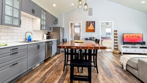 A modern kitchen with grey cabinets, a wooden dining table, and a TV in the living area. - Pet & Family Friendly, Mountain Views, Downtown Montrose 20 Min to National Park (Montrose)