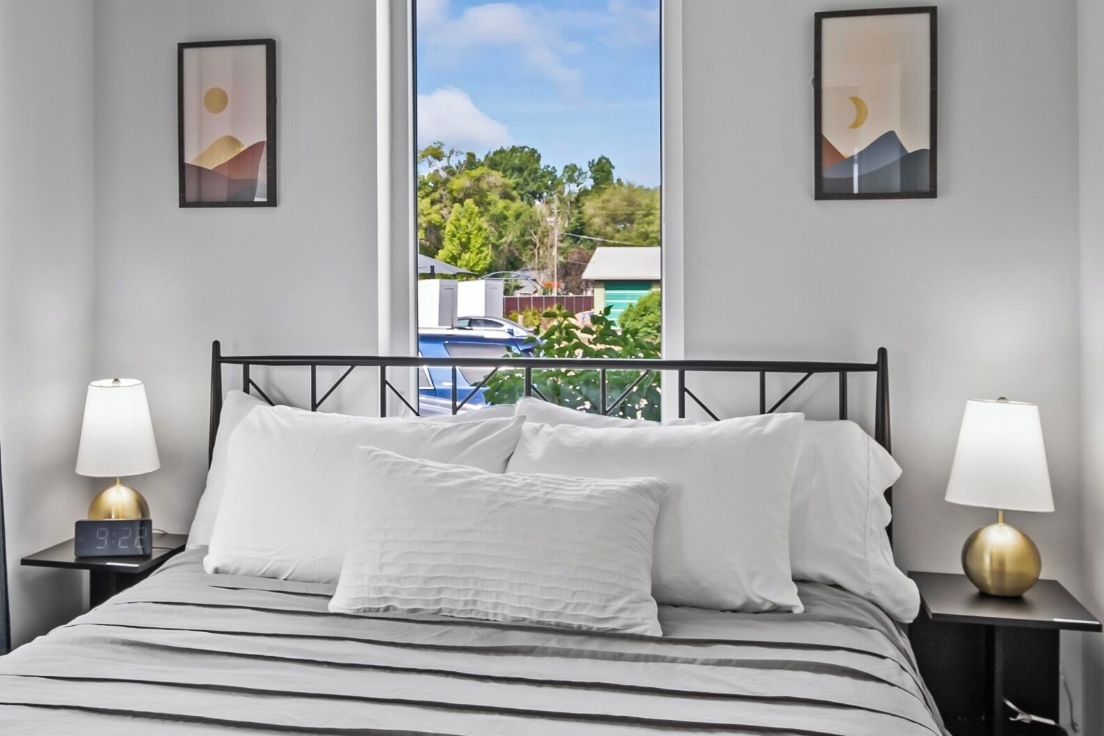 A hotel room with a bed, two bedside tables with lamps, and a window with a view of greenery and a building.