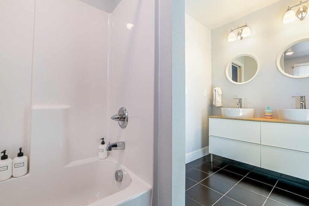 A modern bathroom with a bathtub, two sinks, and a mirror.