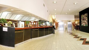 Uma área de recepção de hotel com balcão, posto de informações, telefone e espaço de espera.
