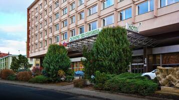 A hotel with a modern facade, a sign indicating it is the Olympic Congress Hotel, and a covered entrance area with trees and shrubs.
