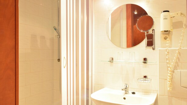 Un baño con cabina de ducha de vidrio, un lavabo con espejo y artículos de aseo en una estantería.