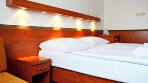 Quarto de hotel com cabeceira de madeira, duas camas, mesa de cabeceira e luminária fixada na parede.