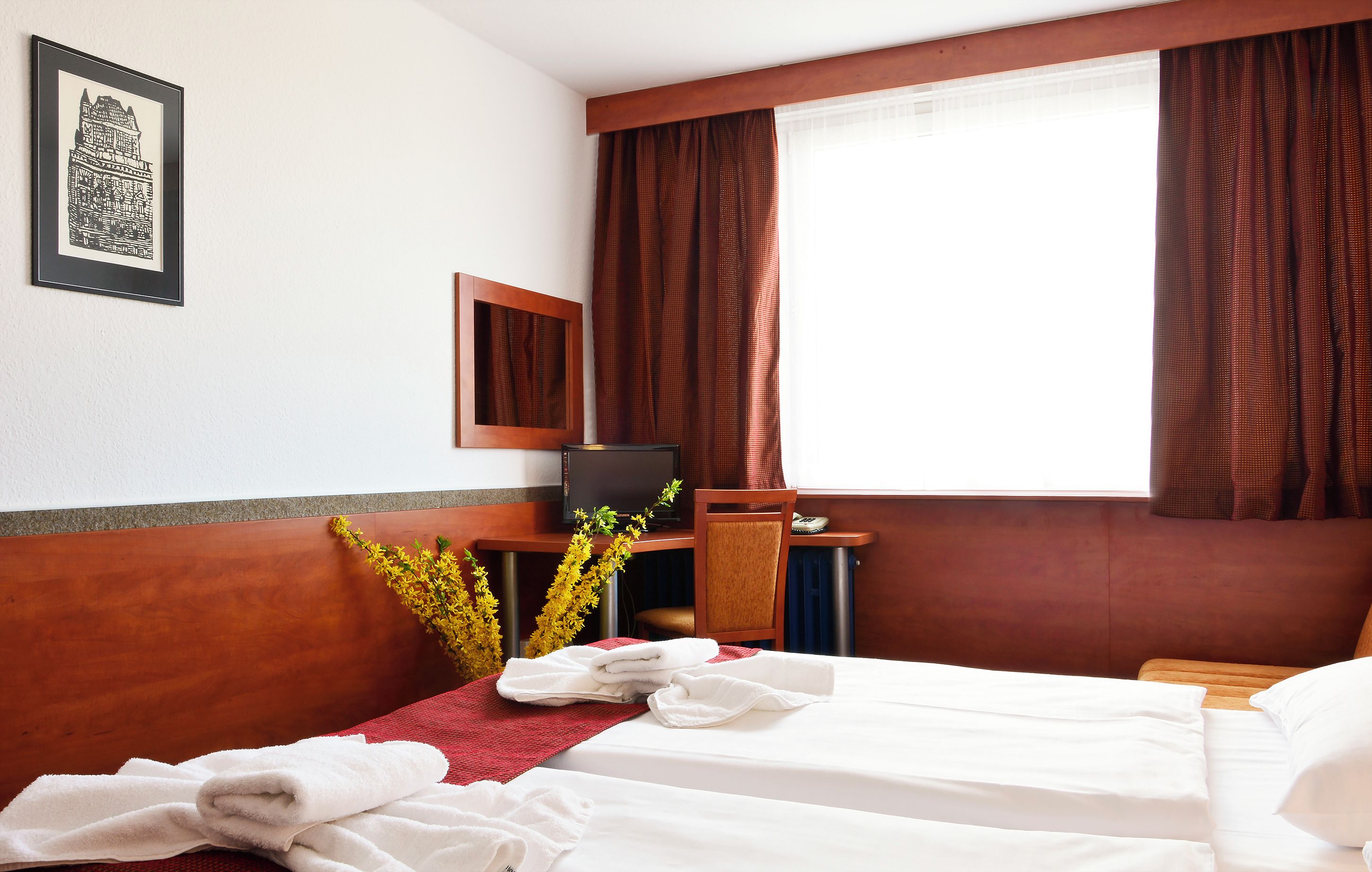 Habitación de hotel con cama, escritorio con computadora, espejo y ventana con cortinas.