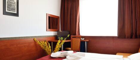 Habitación de hotel con cama, escritorio con computadora, espejo y ventana con cortinas.