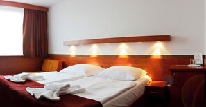 A hotel room with a bed, a nightstand, a desk, and a window with curtains. - Olympik Congress Hotel (Prague)