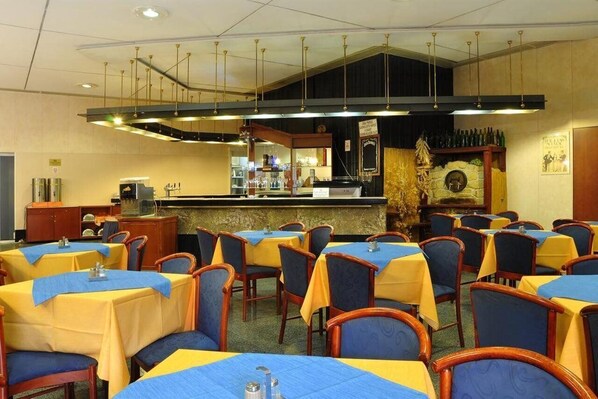 A restaurant with tables covered in blue and yellow tablecloths, wooden chairs, and a bar area with bottles and a stone fireplace. - Olympik Congress Hotel (Prague)