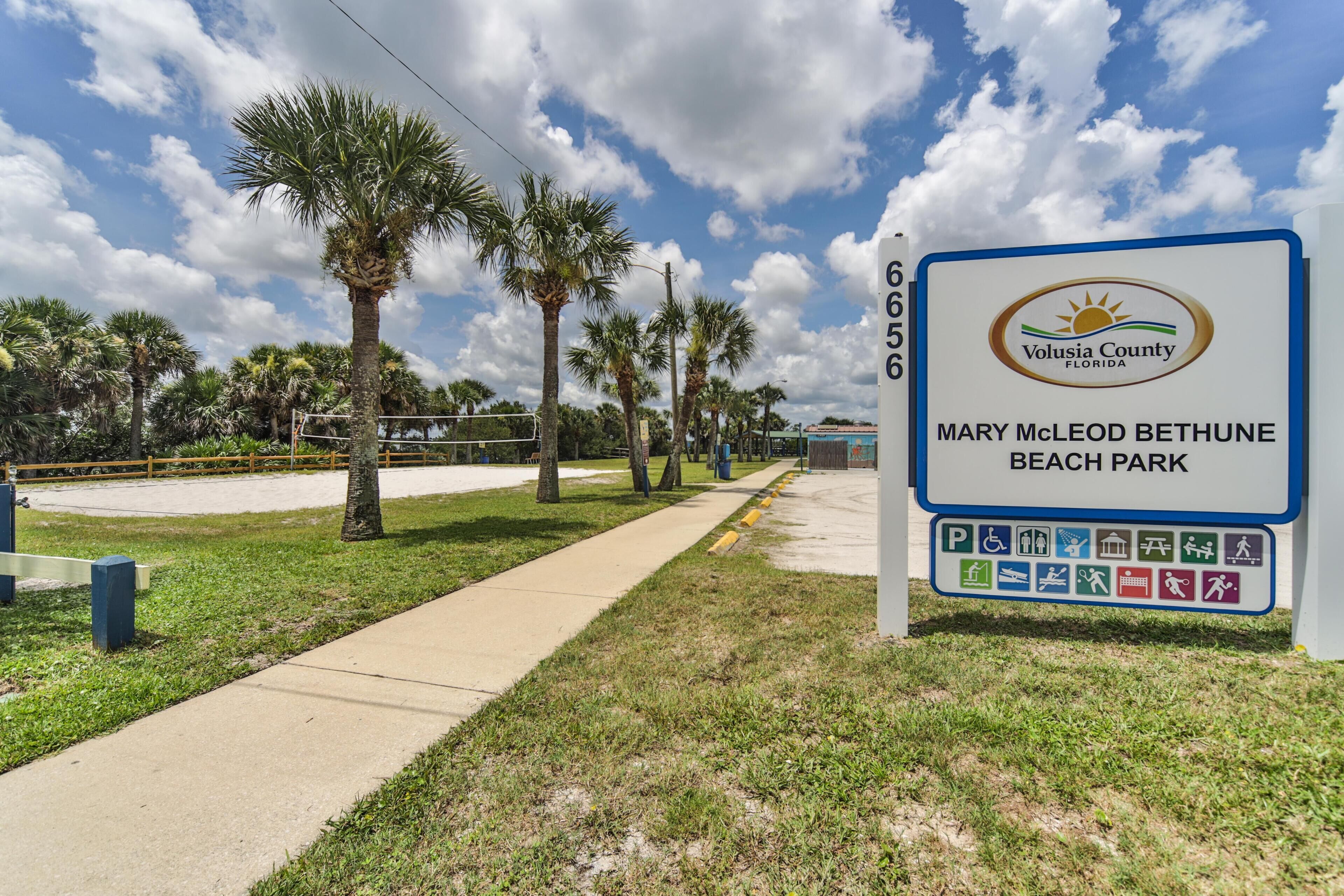 A beach park sign with amenities icons, palm trees, and a clear sky.