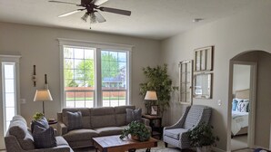 A spacious living room with a sofa set, a coffee table, a patterned armchair, and a large window offering a view of the outdoors.