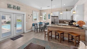 Une cuisine moderne dotée d’un îlot central, d’un coin repas avec vue sur la piscine et d’une décoration sur le thème de la plage.