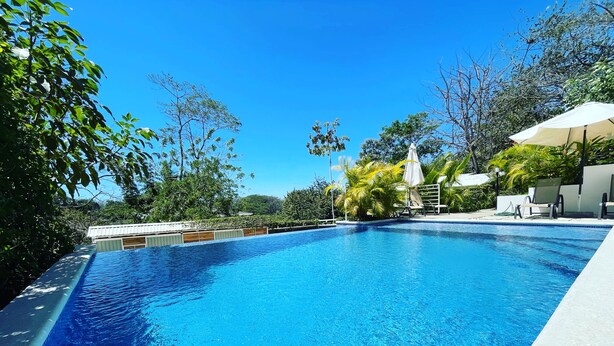 Una piscina cristallina blu circondata da un rigoglioso verde e un ombrellone bianco.