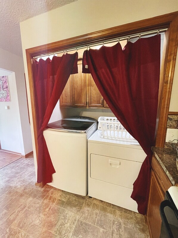 Une petite buanderie équipée d’un lave-linge et d’un sèche-linge, de meubles en bois et d’un sol carrelé.