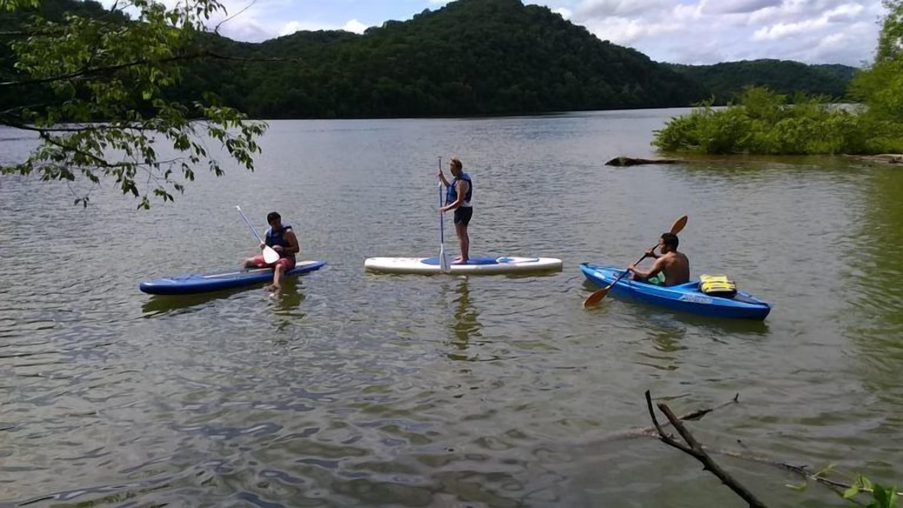 Tre persone su tavole da paddleboard in un lago tranquillo, circondato dal verde.