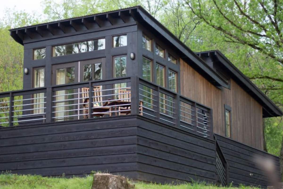 A modern wooden cabin with a balcony, large windows, and a rustic design.