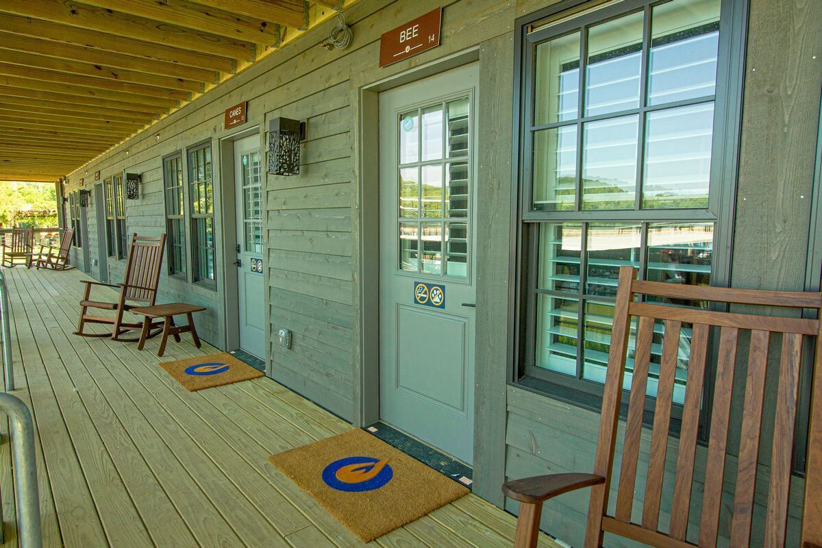 A covered porch with wooden chairs and a bench, a door labeled "BEE 14", and a view of the beach through large windows.