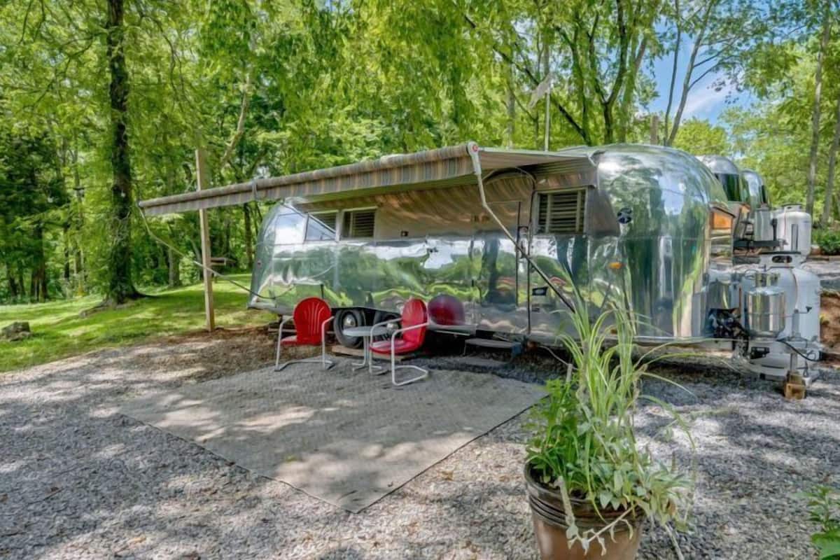 A mobile home with a covered patio area, a small table, and two red chairs.