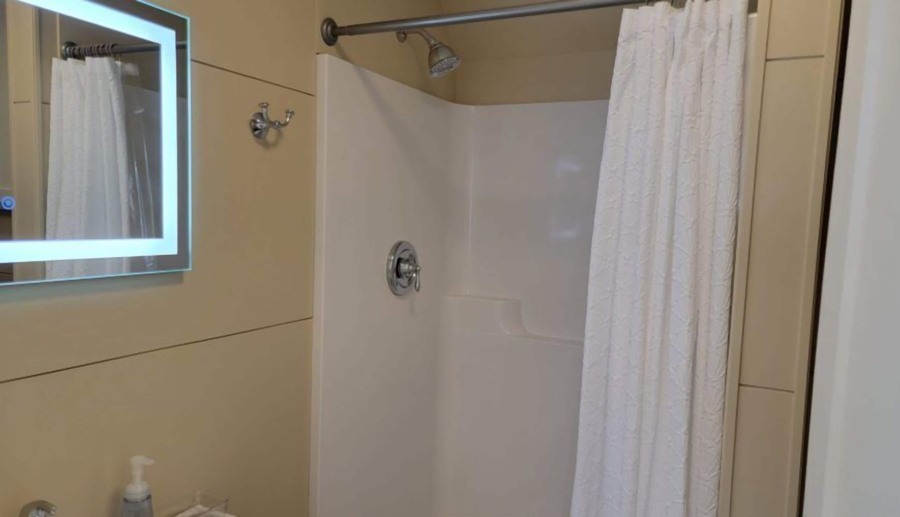 A bathroom with a shower, a mirror, and a hand soap dispenser.