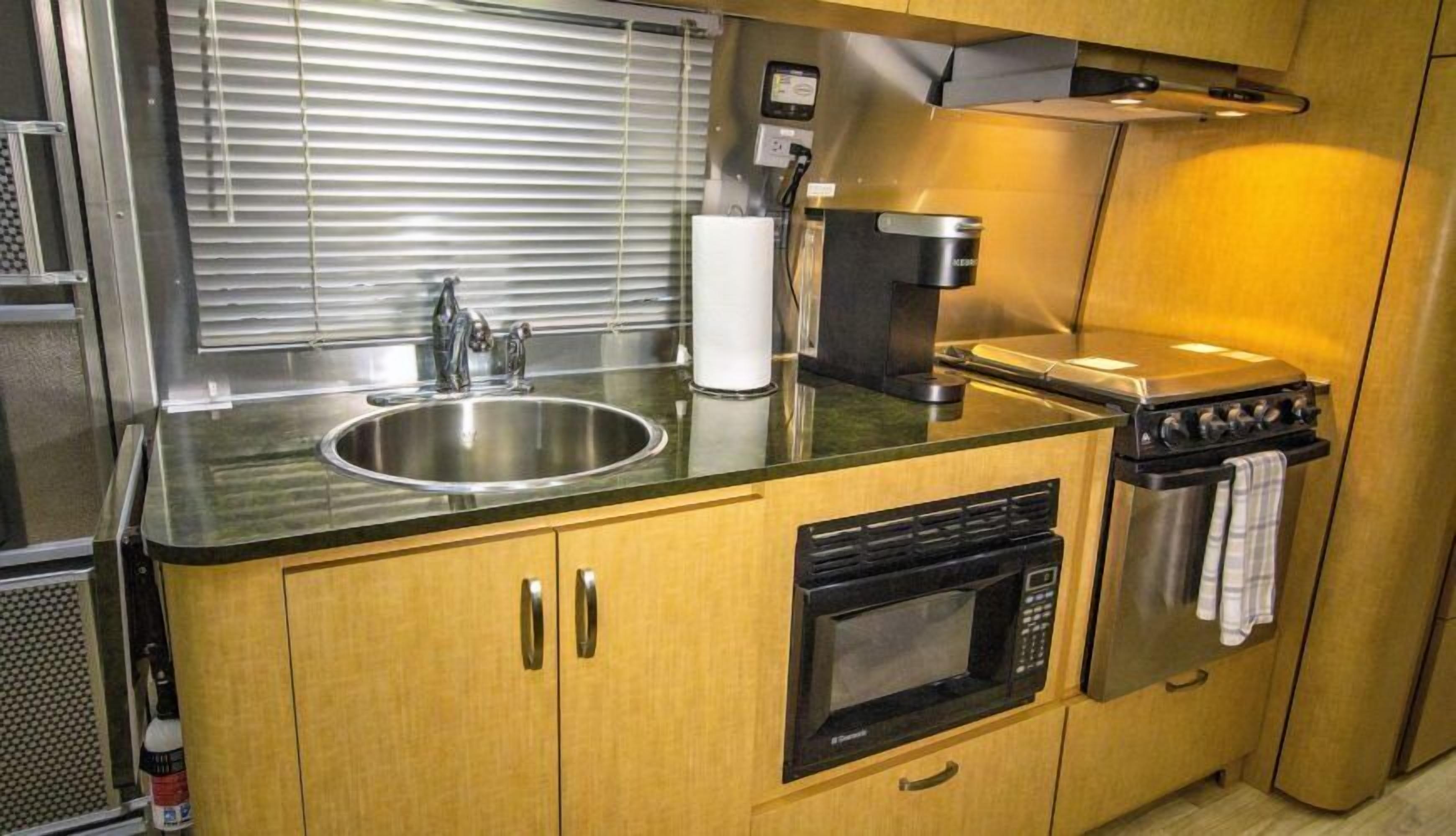 A compact kitchenette with a stainless steel sink, a microwave, a stove, and wooden cabinets.