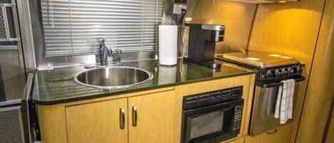 A compact kitchenette with a stainless steel sink, a microwave, a stove, and wooden cabinets.