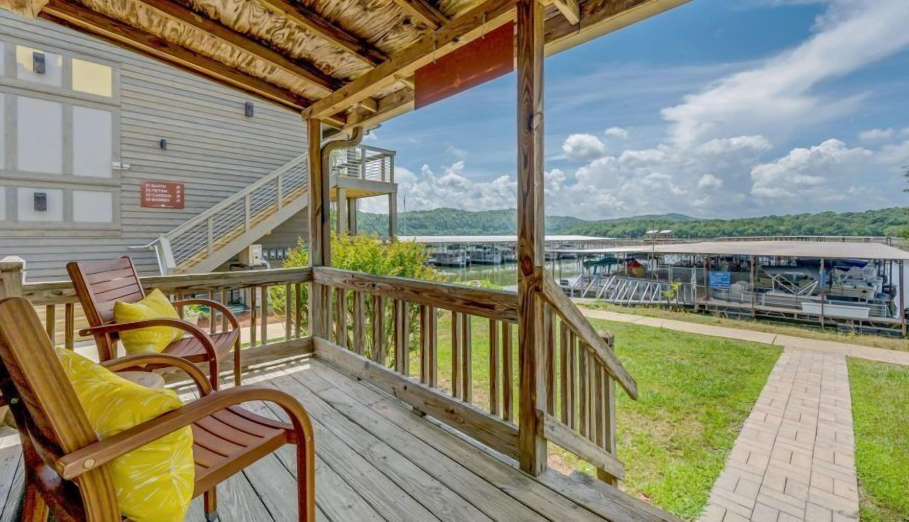 Terraza cubierta con sillas de madera y vista a un muelle y barcos.