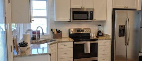 A modern kitchen with white cabinets, stainless steel appliances, a granite countertop, and a window providing natural light.