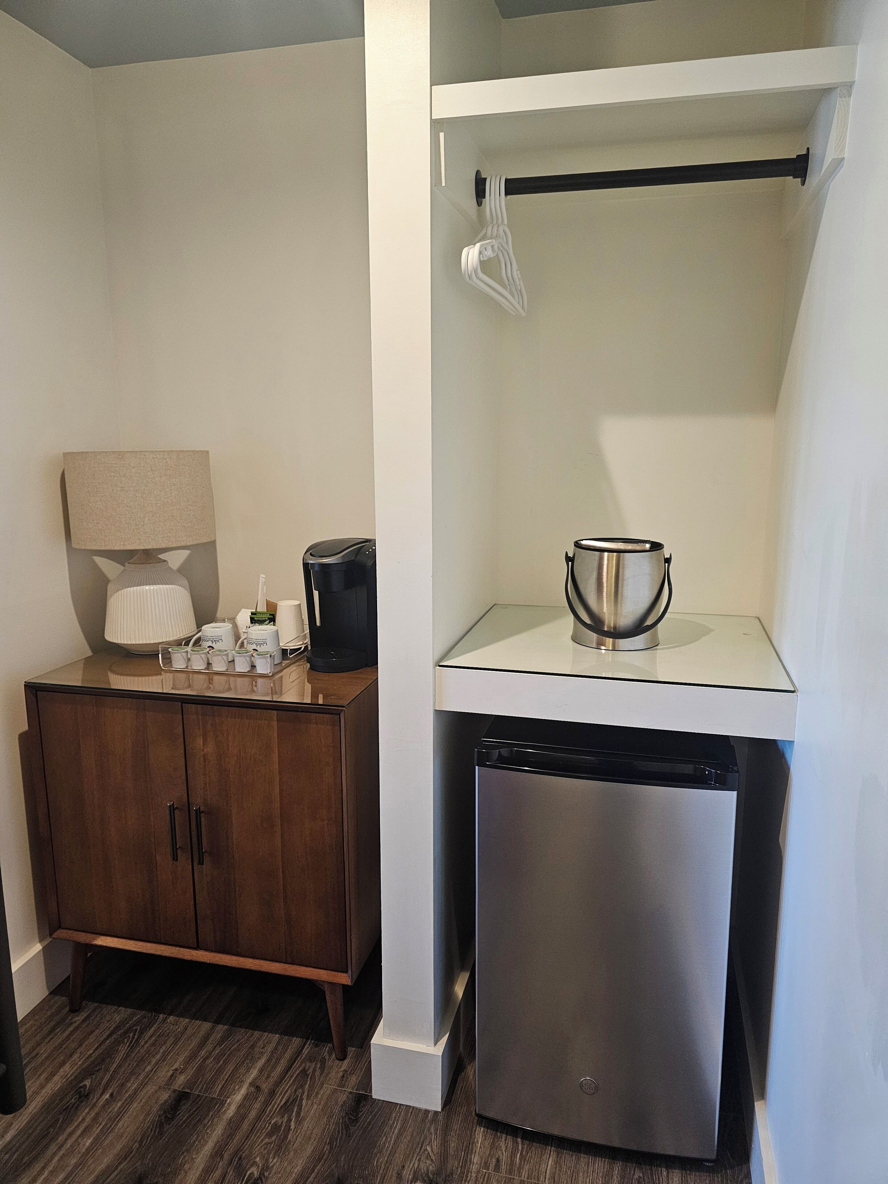A compact kitchenette with a wooden cabinet, a coffee maker, a kettle, and a dishwasher.