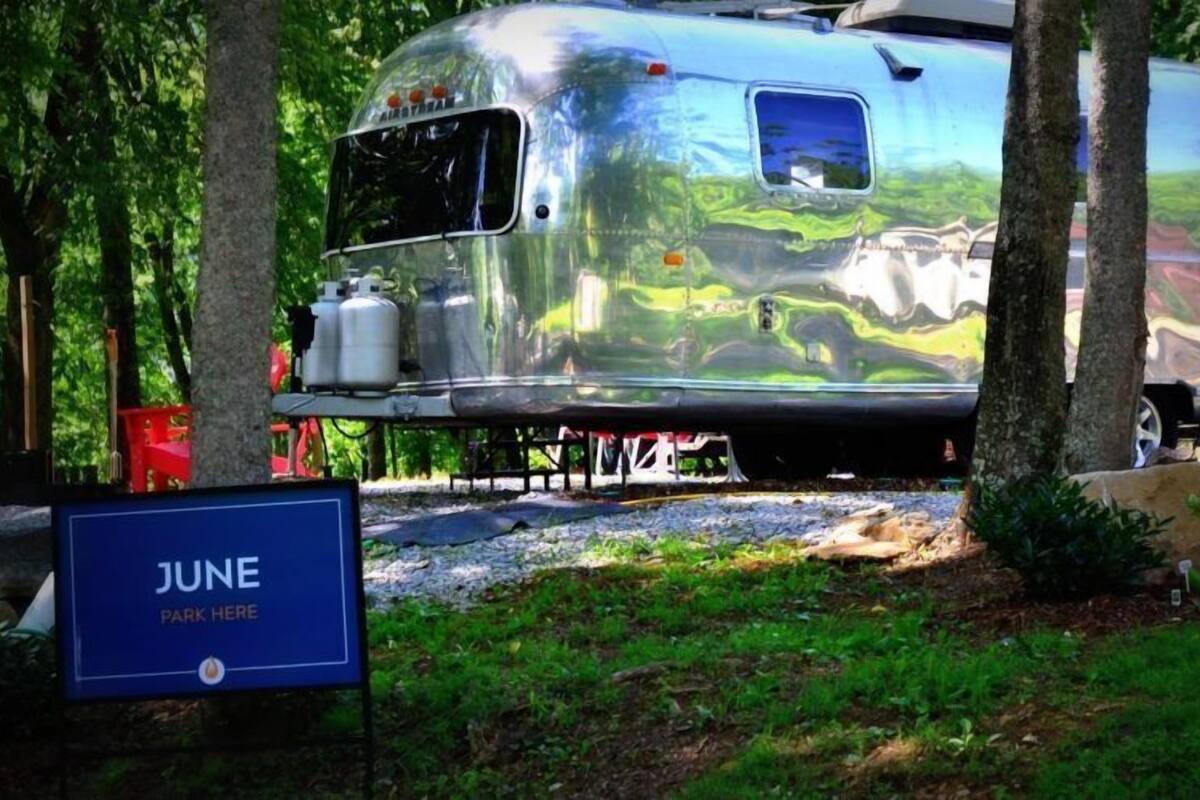 A silver RV parked in a wooded area with a sign indicating 'JUNE PARK HERE'.